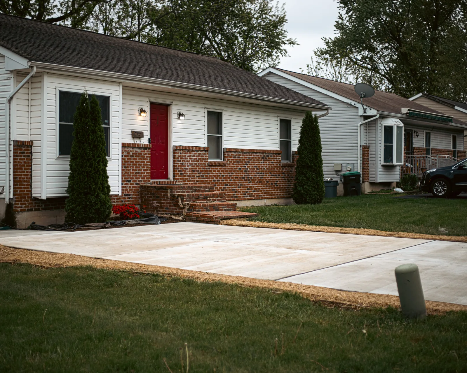 Concrete driveway leading to a brick home with red door in New Castle, DE