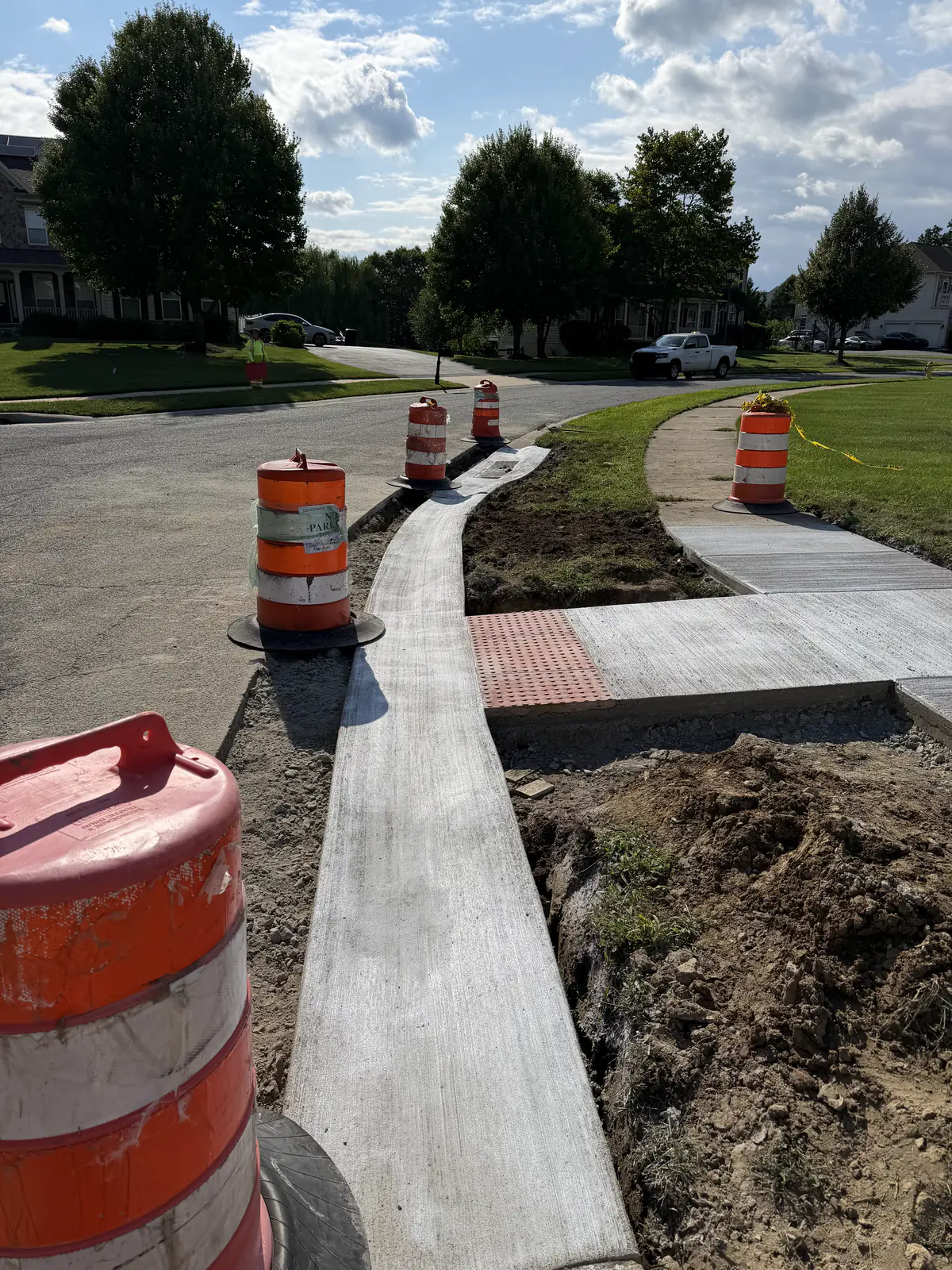 New concrete sidewalk, curb, and ADA ramp with a detectable warning pad under traffic control in a New Castle County, DE subdivision