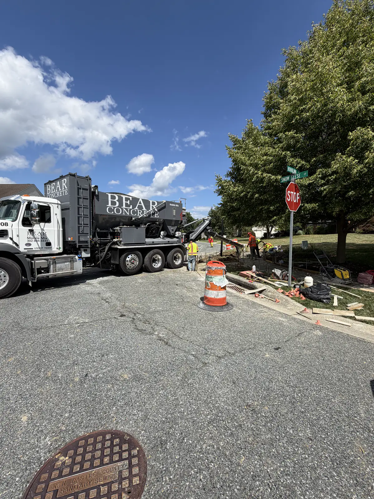 Mobile mix concrete truck and hi-vis crew placing curb and sidewalk at a New Castle County, DE intersection