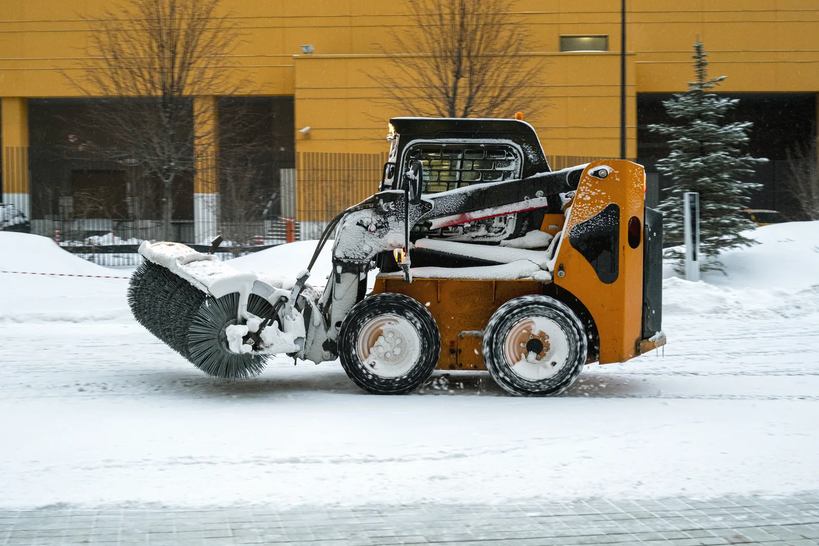 Skid steer loader clearing snow from a paved surface in winter